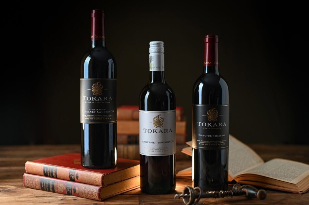 Three Tokara Cabernet Sauvignon bottles — Reserve Collection, Cabernet Sauvignon and Director's Reserve — on a wooden table with old books and a corkscrew